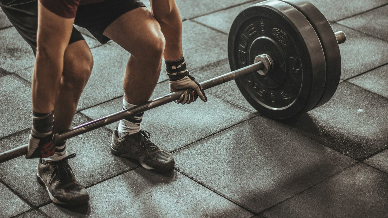 A man gripping a loaded barbell on a gym floor, about to deadlift